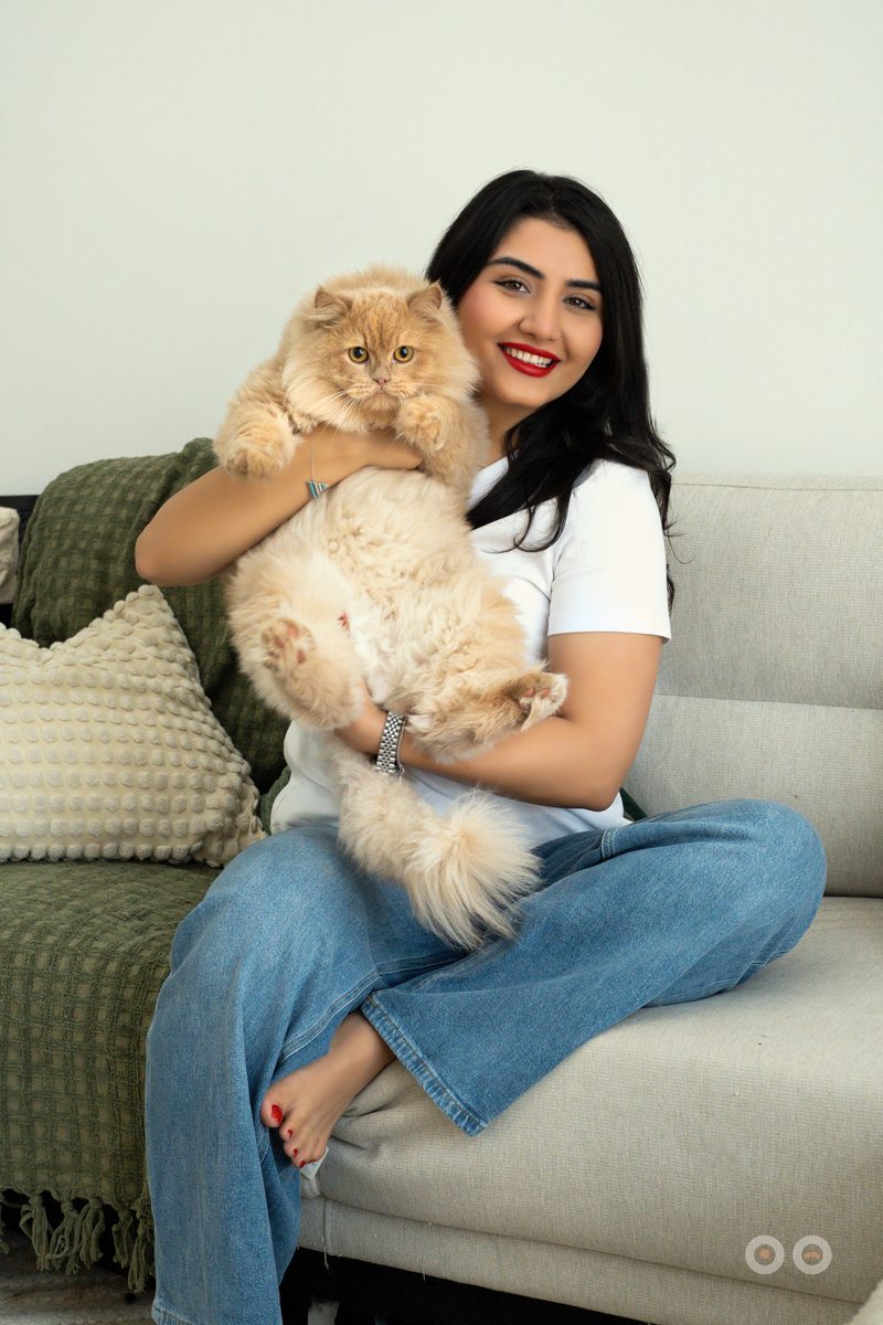 A woman holding her long-haired cat on the sofa at home.